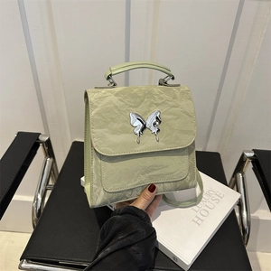 Sac à main vert pistache en cuir plissé avec boucle papillon argentée sur une chaise en cuir