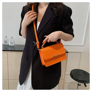 Detail of bright orange crocodile pattern handbag with gold clasp on a model