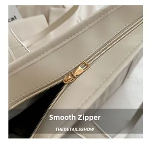 Close-up of smooth gold metal zipper and stitching detail on cream leather tote bag