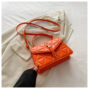 Detail of quilted orange leather handbag with gold belt buckle on a blazer background