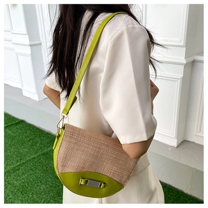 Detail view of straw crossbody bag with green leather trim on a model against white wall