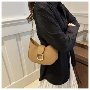 Detail of camel leather saddle bag featuring a gold D-ring buckle and metal chain strap