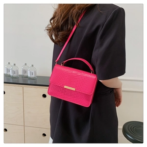 Detailed view of magenta crocodile pattern handbag with gold hardware on a shoulder strap