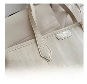 Close-up of beige tote bag featuring textured embossed leather and brand logo detail