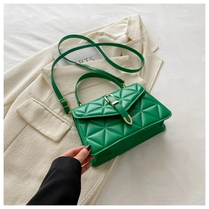 Detail of green quilted handbag with gold buckle and adjustable strap on beige suit