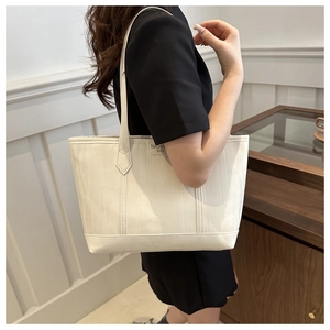Close-up of white tote bag with vertical textured stripes and minimalist leather logo detail