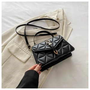 Detail of black quilted crossbody bag with golden buckle on a beige blazer background
