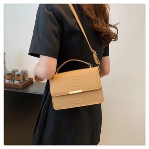 Detail of khaki snake pattern leather handbag with gold metal clasp on black dress