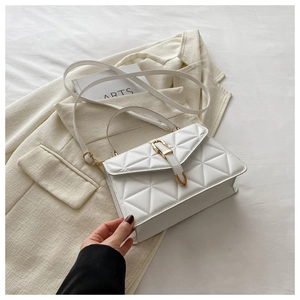 Detail of white quilted crossbody bag with golden buckle on elegant white suit background