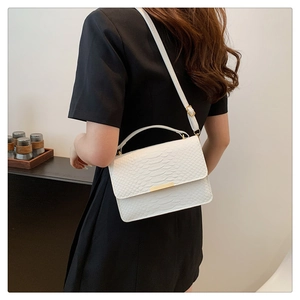 Close-up of white crocodile texture leather handbag with gold metal bar and top handle