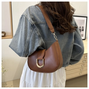 Detailed shot of a brown saddle shoulder bag with a gold D-buckle on a stylish model