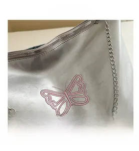 Close-up of pink butterfly embroidery on silver metallic PU crossbody bag with chain strap