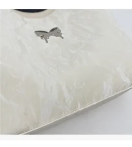 Macro detail of creamy white wrinkled faux leather bag with silver butterfly hardware