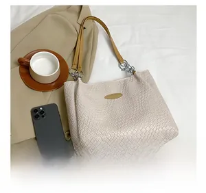 Detail of a woven cream tote bag featuring tan handles and metallic chain links
