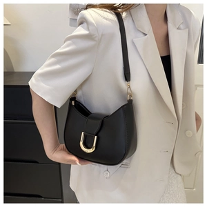 Detail of a black crescent shoulder bag with a gold U-shaped buckle on a model