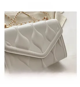 Macro detail of white quilted crossbody bag with golden metal chain strap and flap design