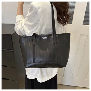 Detail of black faux leather tote bag with zebra texture and branded label on model's shoulder