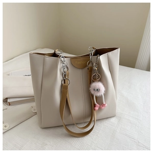 Dettaglio della borsa tote crema con spalline in pelle marrone e ciondolo pompon rosa