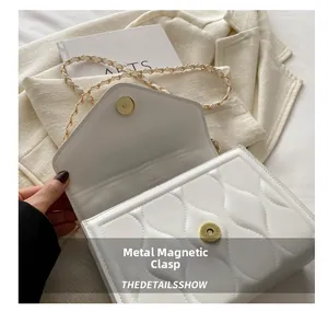 Close-up of white quilted crossbody bag with gold magnetic buckle and chain strap