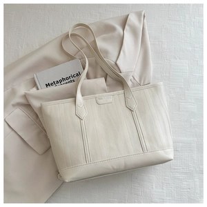 Close-up of cream tote bag with wave-textured leather and branded logo patch
