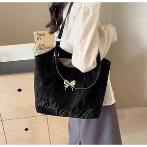 Detail of a large black tote bag with silver butterfly charm shown on shoulder