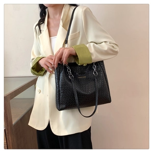 Detail of black woven texture tote bag featuring golden lettering and metal ring handle