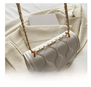 Detail of gold metal chain strap on a white quilted crossbody bag with wave pattern