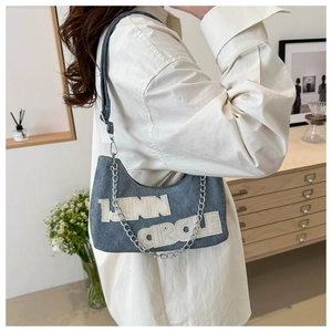 Detail of blue denim underarm bag with white LINN CIRCLE lettering and chain strap