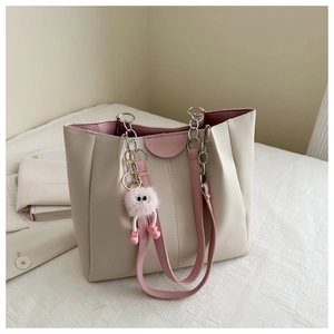 Dettaglio della borsa tote crema con charm mostro rosa su letto bianco testurizzato