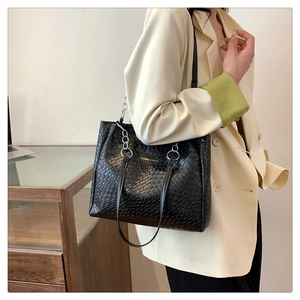 Close-up of black crocodile pattern tote bag featuring a silver metal logo and chain detail