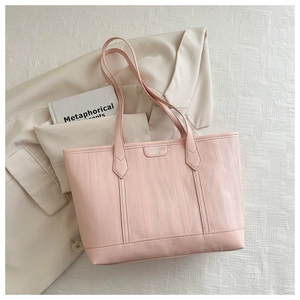 Detail of pink faux leather tote bag with wavy embossed texture and metal logo plaque