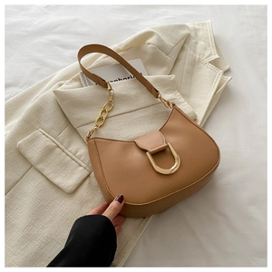 Detail of camel crescent shoulder bag with golden D-ring buckle and chain strap on white fabric