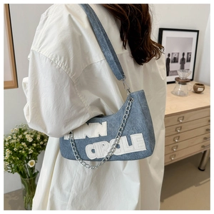 Detail of blue denim shoulder bag featuring bold white INN CIRCLE letters and silver chain