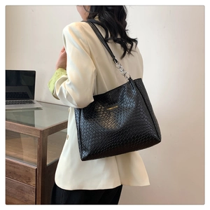 Detail of black woven tote bag with silver chain strap and circular metal logo plaque