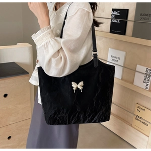 Detail of black pleated tote bag featuring a silver butterfly charm for daily commute