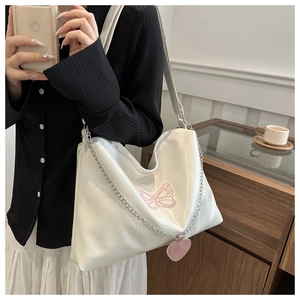 Detailed shot of white shoulder bag with pink butterfly embroidery and heart pendant