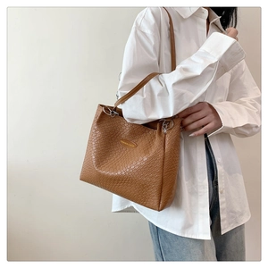 Detail of a brown woven tote bag featuring a gold metal emblem with fashion engraving