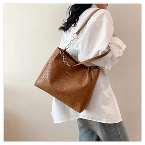 Detailed texture of brown woven tote bag with silver chain and leather shoulder strap