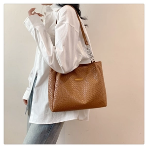 Detail of brown woven tote bag with silver chain strap and oval metal brand logo tag