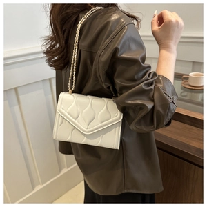 Detailed view of cream quilted envelope bag with gold chain strap on a model