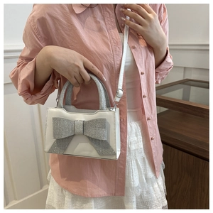 Gros plan d'un mini sac à main blanc avec nœud en paillettes argentées sur tenue