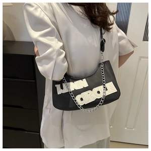 Detailed view of black underarm bag with white letter patch and silver chain strap