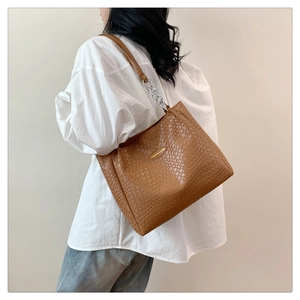 Detail of dark brown tote with crocodile embossed texture and metal chain strap