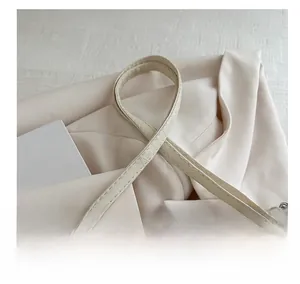 Detail of cream leather shoulder strap with silver buckle and chain on a modern handbag