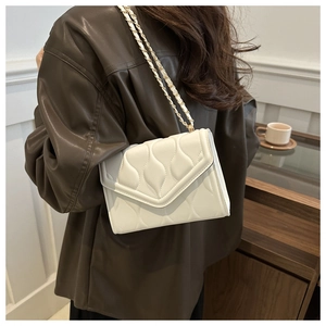 Detail of cream quilted crossbody bag featuring wave patterns and gold chain strap