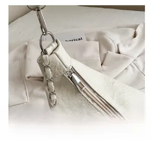 Close-up of smooth silver zipper and chain strap on off-white textured faux leather bag