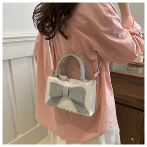 Détail d'un sac à main blanc avec un grand nœud en strass porté par un mannequin en tenue