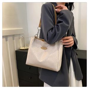 Detail of cream crocodile embossed shoulder bag with slim brown handles and metal rings