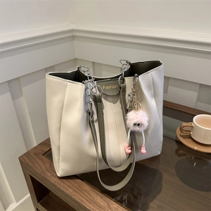 Elegante borsa tote crema con manici verde scuro e un ciondolo rosa sul tavolo