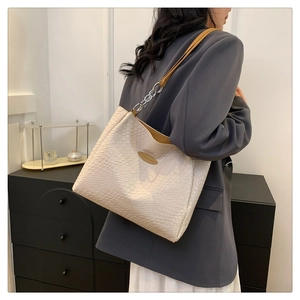 Detail of off-white woven tote bag with silver chain strap and brown leather accent